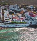 Colorful hillside coastal town with multicolored apartment buildings above a turquoise sea and rocky hills in the background.
