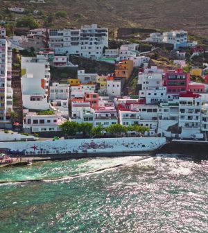 Colorful hillside coastal town with multicolored apartment buildings above a turquoise sea and rocky hills in the background.