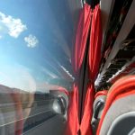 Viewing countryside while traveling with bus | Upitravel Bus interior with red curtains and red seats, window showing highway and hills outside.