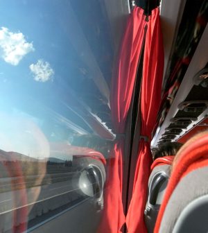 Bus interior with red curtains and red seats, window showing highway and hills outside.
