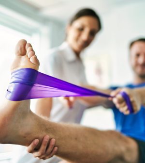 physiotherapist doing treatment with patient in bright office | Upitravel Therapist assists a patient in a leg stretch using a purple resistance band.