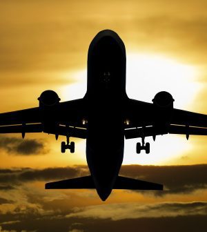 Front-on silhouette of a large passenger jet with landing gear down, against a golden sunset.