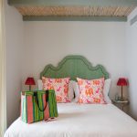 El Escondite - IP | Upitravel White bed with a green arched headboard, coral-patterned throw pillows, and a colorful striped tote on the duvet.