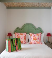 El Escondite - IP | Upitravel White bed with a green arched headboard, coral-patterned throw pillows, and a colorful striped tote on the duvet.